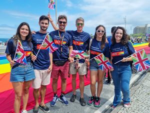 Group of six people wearing matching 'Great Love is for Everyone' shirts holding rainbow and UK flags at UK's Great Love campaign in Copacabana Beach, Rio de Janeiro (2023)